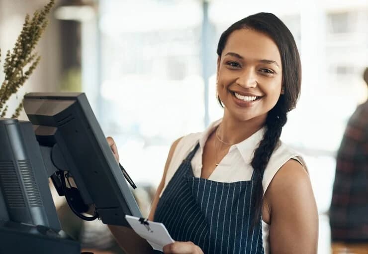 Smiling cashier at a POS terminal in a café, holding a receipt