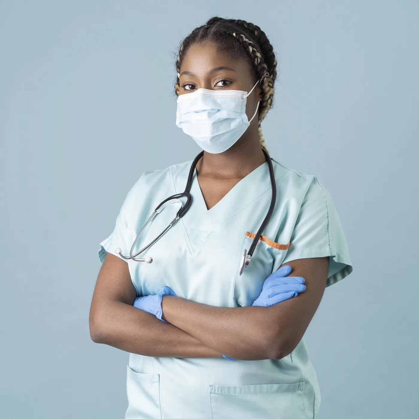 Health worker in scrubs, a face mask and gloves with a stethoscope around her neck, arms crossed